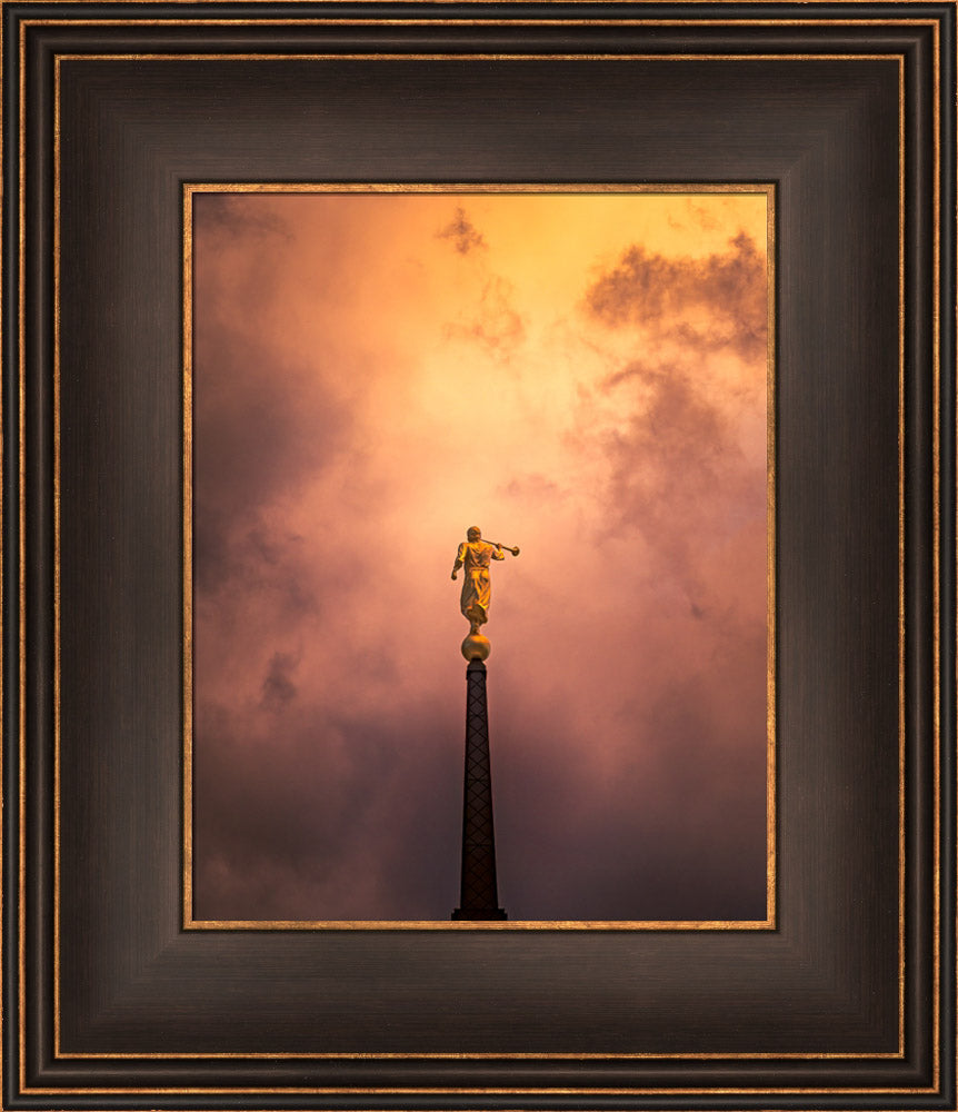 The spire and angel Moroni statue of the Saratoga Springs Utah temple with a cloudy sunset background.