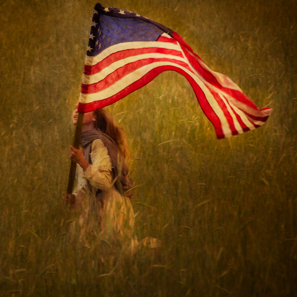 A young girl running through a field waving the American flag.