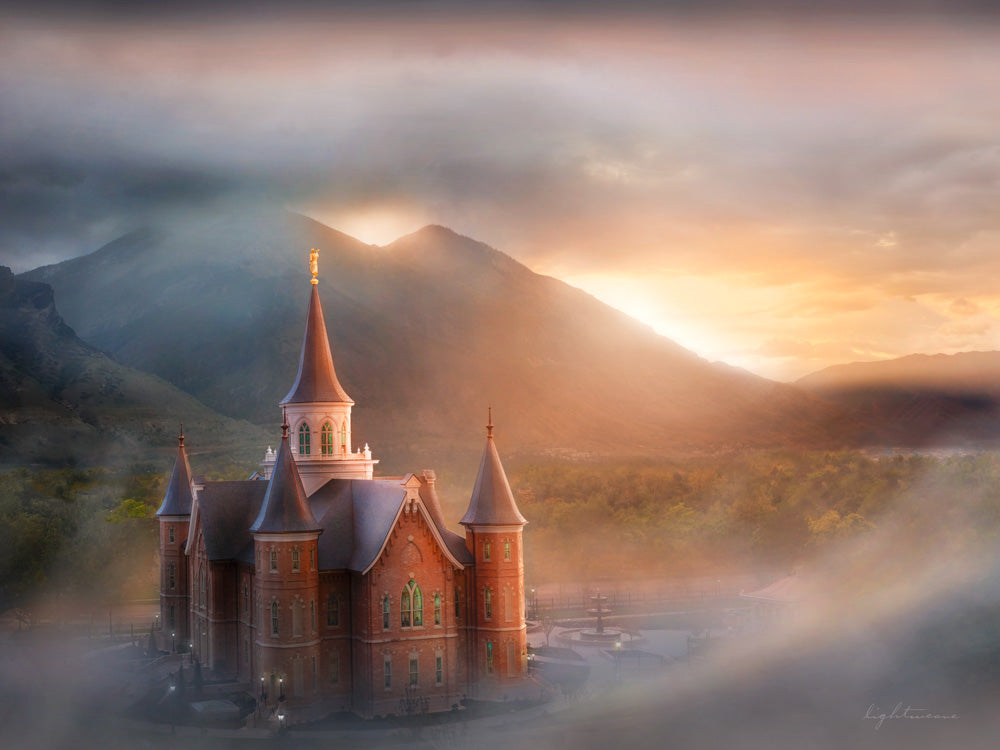 Provo City Center Temple with fog and sun shining behind mountains.