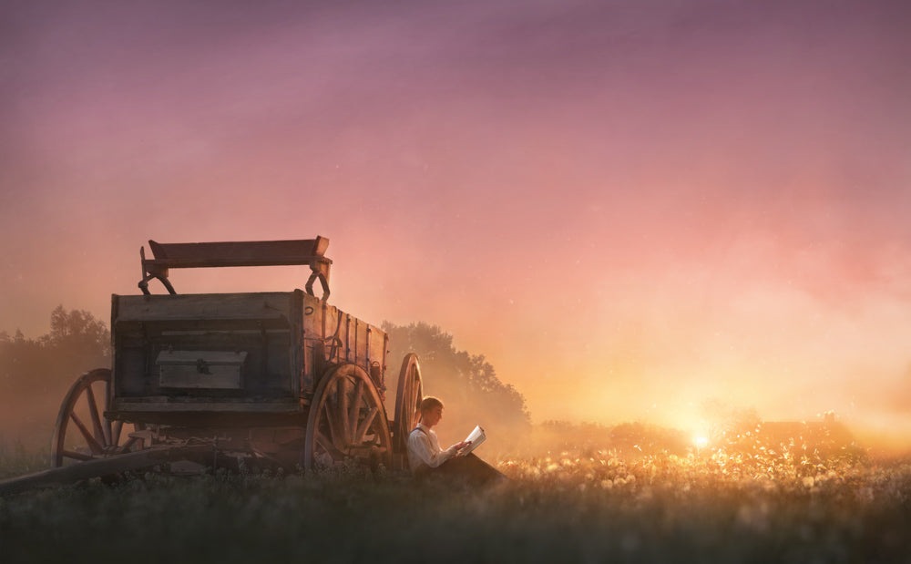 Young Joseph Smith sitting by a wagon reading at sunset.