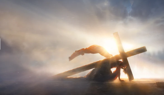 A person carrying a large wooden cross under a dramatic sky with rays of light breaking through clouds.