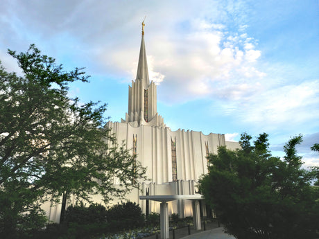 The Jordan River Utah Temple with trees and clouds.