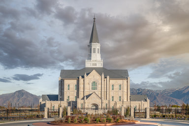 The Taylorsville Utah Temple with gray clouds and mountains.
