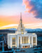 The Saratoga Springs Utah temple lit up against a blue landscape with a pink and yellow sky.