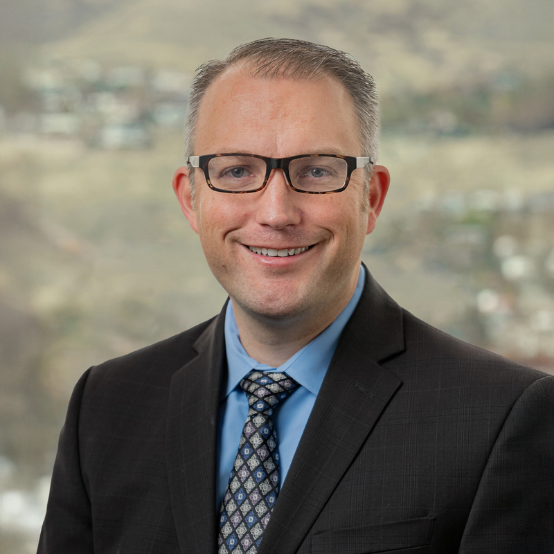 Man wearing glasses and a suit with a blurred landscape background