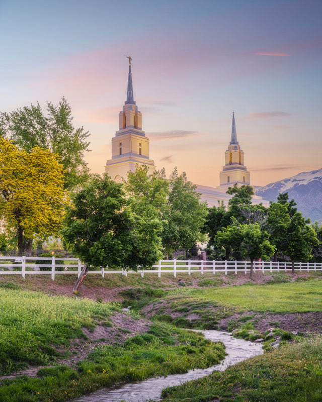 The Layton Utah Temple at sunrise with trees and mountains.