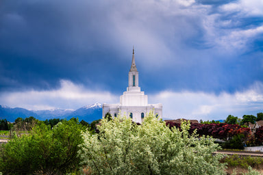 The Orem Utah Temple with a cloudy blue sky and green foliage.