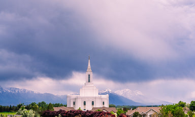The Orem Utah Temple with a cloudy blue sky and mountains.