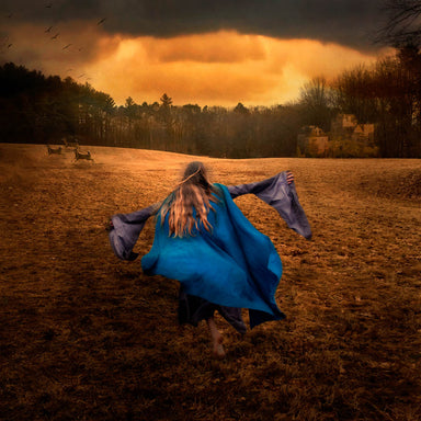 A young woman in a blue dress and cloak runs forward across a forest meadow.