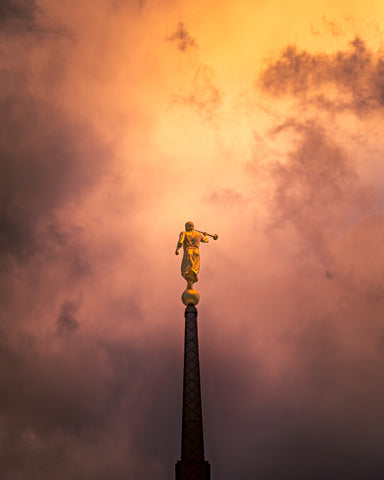 The spire and angel Moroni statue of the Saratoga Springs Utah temple with a cloudy sunset background.