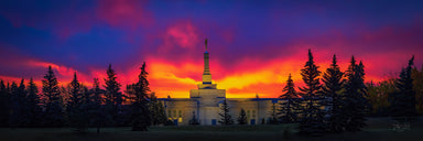 The Edmonton Alberta temple surrounded by trees below a vivid sunrise.