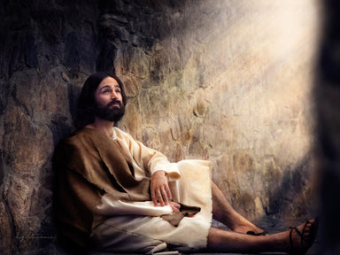 Jesus sitting against a wall with light shining down.