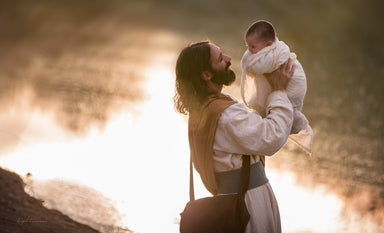Jesus holding up a baby and smiling. 