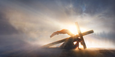 Jesus collapsing beneath the cross. Light shines starkly against the sillouhette of the cross.